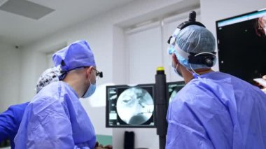 Nörocerrahlar ve anestezi uzmanı röntgen taramasıyla ekipman ekranına bakarak iletişim kuruyor. Profesyoneller ameliyattan önce hazırlanıyor..