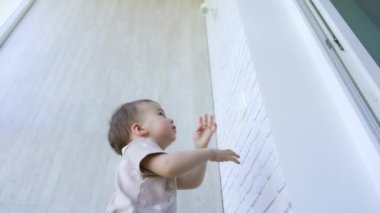 Küçük çocuk duvardaki lambaya ulaşmak istiyor. Komik çocuk bir şey yapıyor ve sonra kamerada dikkatini dağıtıyor..