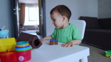 Küçük masada oturan sevimli koyu renk saçlı çocuk. Bebek masada yatan oyuncaklara bakar..