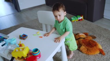 Beyaz masanın yanında duran tapılası çocuk. Güzel çocuk renkli bardaklara minik oyuncaklar koyar. Üst görünüm.