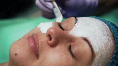 Kadın yüzüne beyaz yüz maskesi takmak. Mavi şapkalı kadın güzellik uzmanında yüz bakımı yapıyor. Çok yakın çekim..
