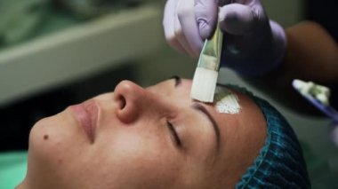 Lastik eldivenli güzellik uzmanı, müşterinin yüzünü maskeyle kaplamak için fırça kullanıyor. Güzellik salonunda gençleştirme prosedürleri. Kapat..