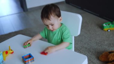 Sevimli çocuk masada oturan oyuncaklarla oynuyor. Güzel bebek renkleri ve şekilleri öğreniyor. Üst görünüm.