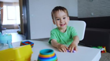 Aktif, sağlıklı, beyaz bir bebek masada oturuyor. Çocuk oyuncakları ve çığlıkları tutuyor..