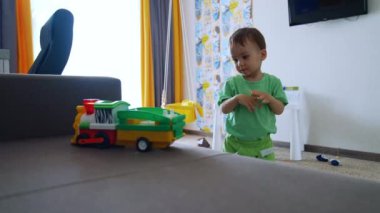 Yeşil elbiseli küçük güzel çocuk odada oynuyor. Küçük çocuk kanepenin yanındaki trene bakıyor..