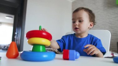 Renkli piramidi birleştiren sevimli çocuk. Koyu saçlı çocuk küçük ellerindeki oyuncağın yüzüklerini takıyor..