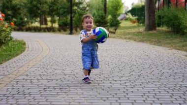 Güzel, heyecanlı bir erkek bebek elinde top tutuyor. Çocuk topu fırlattı ve arkasını döndü. Parkta yaz eğlencesi.