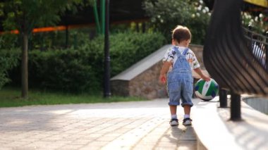 Baloya dikkatle yaklaşan bir erkek bebeğin arka görüntüsü. Sevimli çocuk eline bir top alıp mutlu bir şekilde koşuyor. Düşük açı görünümü.