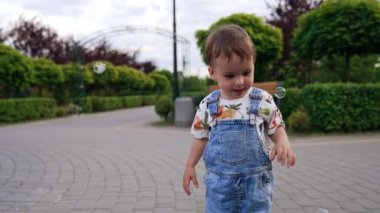 Tatlı küçük bebek sabun köpüklerine bakıyor. Çocuk parkta baloncukları yakalamaya çalışıyor..