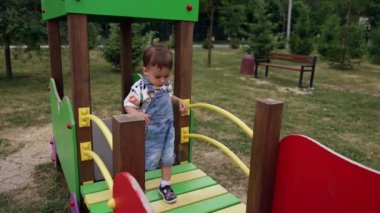 Beyaz çocuk oyun parkındaki ahşap köprünün yanından geçiyor. Küçük çocuk yazın dışarıda vakit geçiriyor..