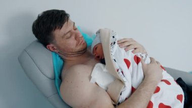 Çıplak göğsü olan kaslı beyaz bir adam yeni doğan bebeğini tutuyor. Hastanede doğan bir çocuk için cilt teması..