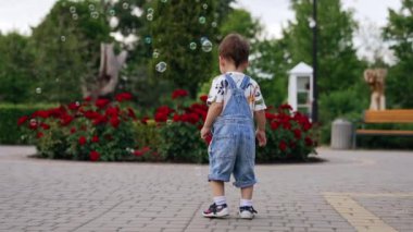 Kot pantolon giymiş sevimli bir bebek sabun köpüğüyle oynuyor. Mutlu çocuk yazın parkta oynuyor..