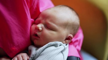 Güzel beyaz bebek annesinin kollarında uyuyor. Bakıcı anne oturur ve yeni doğan çocuğunu sallar. Kapat..