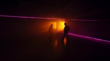 Karanlık stüdyoda dans eden birkaç siluet. Modern tarz performans. Arkaplanda sarı lamba ve pembe neon ışık.