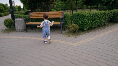 Koyu renk saçlı, kot pantolonlu bir çocuk ahşap bir bankta koşuyor. Çocuk bankın yanında duruyor ve koşmaya devam ediyor..
