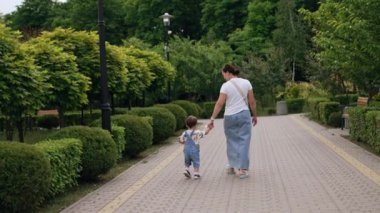 Parkta el ele tutuşan bir anne ve oğlunun arka görüntüsü. Elinde kova, elinde kürek tutan bir çocuk.