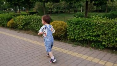Yolda koşan kot pantolonlu bir çocuğu takip ediyormuş. Mutlu bebek yaz parkında yürürken.
