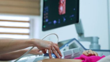 Hamileliğin ilk safhalarındaki beyaz bir kadın için ultrasonik muayene. Arkaplanda ultrason makinesinin monitörü.