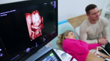 Bebek görüntüsü olan monitör. Kontrol edilen kadın ve kocası arka plandalar. Üst görünüm.
