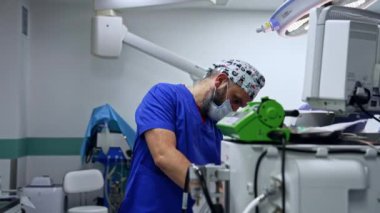Sakallı beyaz doktor maskesini yüzüne takıyor. Anestezi uzmanı ameliyathanede çalışan bir ekipmana geliyor..