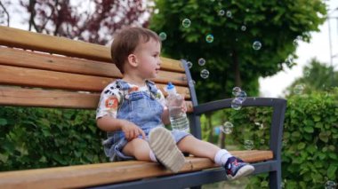 Beyaz, şirin bir çocuk elinde su şişesiyle bankta oturuyor. Tatlı çocuk etrafta uçuşan sabun köpüklerinden mutlu ve onları yakalamaya çalışıyor..