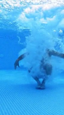 Adam havuzda suyun altına atlar. Suya atlayan ve yüzme havuzunda yüzen bir adamın sualtı görüntüsü. Dikey video