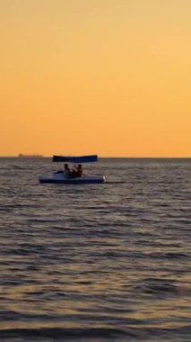 Gün batımında deniz kenarında katamaran. Akşamları mavi bir katamaranla denizde yelken açan adamlar. Dikey video