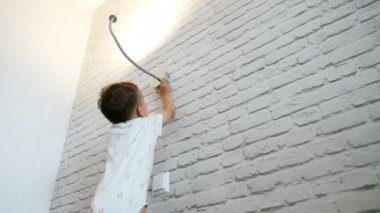 Sevimli beyaz çocuk duvardaki lambaya uzanıyordu. Bebek evde ışıkla oynuyor. Düşük açı görünümü.