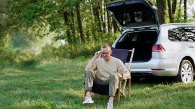 Katlanan sandalyede oturan rahat adam gözlük takıyor. Freelancer bilgisayarını alır, açar ve çalışmaya başlar. Doğa zemin.