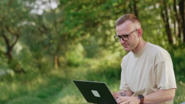 Meşgul adam doğal çevrede çalışıyor. Freelancer dizüstü bilgisayara bakar..