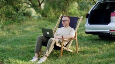 Serbest çalışan erkek, dizüstü bilgisayarla katlanır bir sandalyede oturuyor. Doğada uzaktan çalışan serbest çalışan biri..