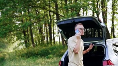 Gözlüklü adam arabasının yanında yürüyor ve telefonda konuşuyor. Tatilde iş meselelerini çözmek.