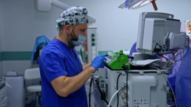 Erkek anestezi uzmanı ameliyathanedeki ekipmanı çalıştırıyor. Tıbbi infüzyon parametrelerini ayarlayan maske ve eldivenli doktor.