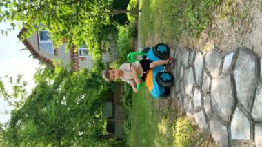 Kafkasyalı erkek bebek oyuncak arabasını neşeyle sürüyor. Yazın dışarıda eğlenmek için. Dikey ekran.