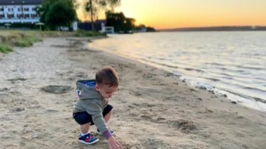 Güzel, beyaz çocuk deniz kıyısında iyi vakit geçiriyor. Bebek kumsaldan biraz kum topluyor..