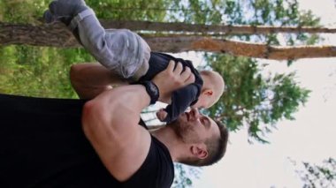 Kafkasyalı mutlu bir adam kucağında küçük bir bebek tutuyor. Sevgi dolu baba küçük oğlunu öpüyor. Doğa geçmişi. Dikey video.