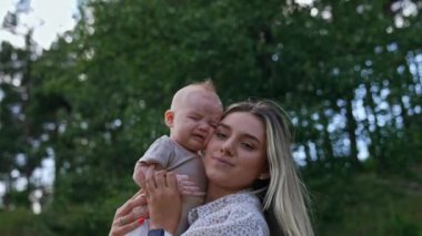 Annesinin yanağına yaslanmış ağlayan küçük bir bebek. Sevimli yeni doğmuş bebek, annesinin onu rahatlattığı gibi acı acı ağlıyor. Doğa arka planda.