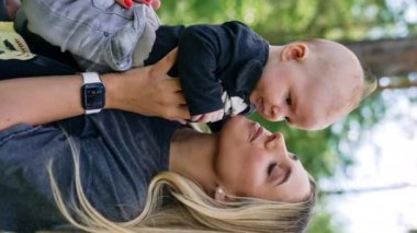 Elinde bebeği olan sarışın bir kadın. Sevgi dolu bir anne çocuğunu yanağından öpüyor. Dikey ekran.