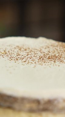 Pastanın beyaz kremalı yüzeyine kakao tozu serpiştirilmiş. Kapatın. Modern şekerleme dükkanındaki kekleri süslüyordum. Dikey video