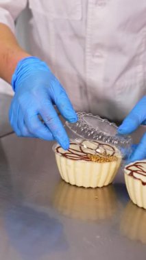 Tatlı kremalı tatlılar paketleme. Lateks eldivenli işçilerin elleri ayrı ayrı plastik kek kutularının kapaklarını kapatıyor. Kapatın. Dikey video