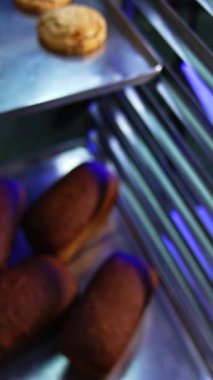 Taze pişmiş küçük kruvasanlarla dolu metal pişirme çarşafı. Kapatın. Modern pastanede tatlı tatlılar üretiliyor. Dikey video