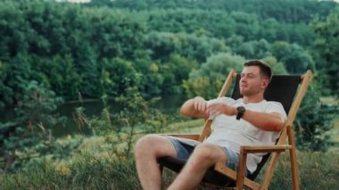 Beyaz tişörtlü mutlu adam laptopuyla işe ara veriyor. Adam ellerini başının arkasına koyar ve bir sandalyede dinlenir..