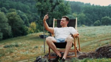 Doğada çalışan serbest çalışan bir adam telefonunda görüntülü konuşma yapıyor. Adam telefonunu kaldırır ve konuşur kayadaki sandalyede oturarak..
