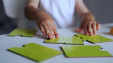 Bulmacalarla oynayan tanınmamış bebeklerin küçük elleri. Çocuk parçaları düzgün birleştirmek için hareket ettiriyor. Kapat..