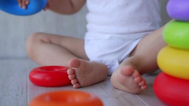 Beyaz takım elbiseli güzel beyaz erkek bebek yerde oturuyor. Çocuk piramitleri birleştirmekle oynuyor. Kapat..
