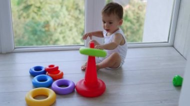 Oyuncak piramidi montajı çok güzel. Beyaz çocuk pencerenin yanında oynuyor..