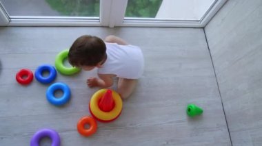 Tatlı erkek bebek oyuncak piramidiyle oynuyor. Çocuk yerde sürünerek gerekli parçaları topluyor. Üst görünüm.