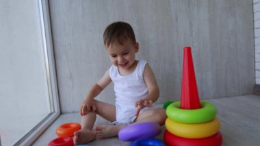 Aktif Kafkas bebek oyuncaklarıyla oynuyor. Bebek çocuk yere oturup oyuncak piramidin yüzüklerini fırlatıyor..