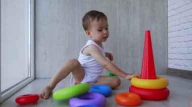 Sevimli aktif bebek oyuncak piramidini söküyor. Çocuk neşeyle renkli yüzükleri çıkarıp yere koyuyor..