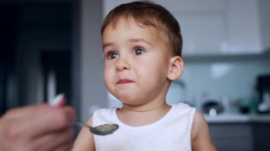 Güzel çocuk yemek yerine konuşur. Annem ona kaşık veriyor ama o bir şey söyleyerek yüz çeviriyor..